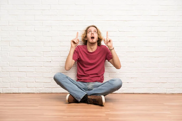 Blonde Man Zittend Vloer Verrast Wijzend — Stockfoto