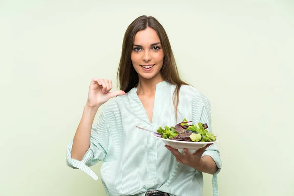 Young woman with salad over isolated green wall proud and self-satisfied