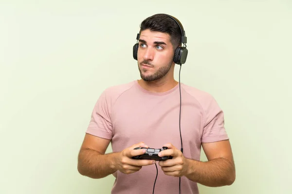 Молодой Красивый Мужчина Играет Контроллером Видеоигры Над Изолированной Зеленой Стеной — стоковое фото