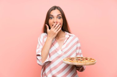 Genç kadın sürpriz yüz ifadesi ile izole pembe duvar üzerinde bir pizza tutan