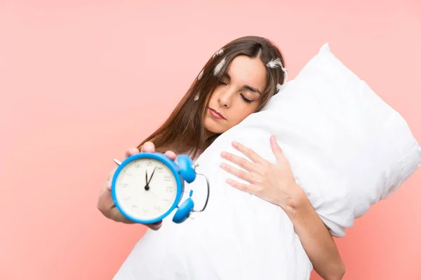 Jeune femme en pyjama sur fond rose isolé tenant horloge vintage — Photo