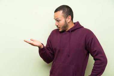 Palmiye üzerinde copyspace hayali tutan yeşil duvar üzerinde sweatshirt ile Kolombiyalı adam