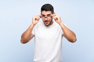 Gözlüklü izole mavi arka plan üzerinde Kafkas yakışıklı adam ve şaşırttı