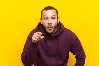 Sarı duvar üzerinde sweatshirt ile Kolombiyalı adam şaşırttı ve ön işaret
