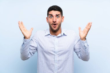 Kafkasyalı yakışıklı, yalıtılmış mavi arka planda, şaşırmış bir yüz ifadesi var.