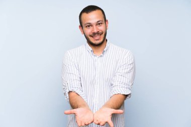 Bir reklam eklemek için palmiye üzerinde izole mavi duvar tutan boşaltmak hayali üzerinde Kolombiyalı adam
