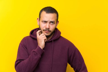 Sarı duvar üzerinde sweatshirt ile Kolombiyalı adam şüpheleri olan