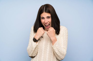 İzole mavi duvar üzerinde genç kadın bir zafer kutluyor