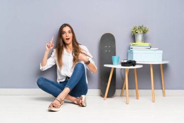 Genç bir kadın yerde oturuyor ve yüzünde sürpriz bir ifade var.