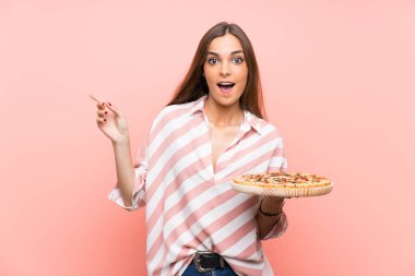 İzole pembe duvar üzerinde bir pizza tutan genç kadın şaşırttı ve yan parmak işaret