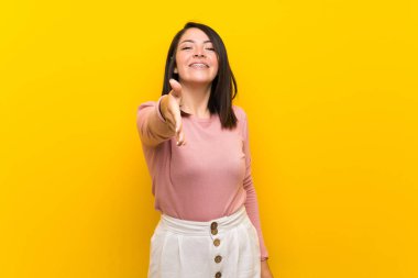 Izole sarı arka plan üzerinde genç Meksikalı kadın iyi bir anlaşma kapanış için el sıkışma