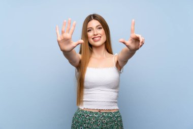 İzole edilmiş mavi arka plan üzerinde genç bir kadın parmaklarıyla yediyi sayıyor