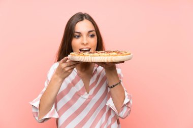 İzole pembe duvar üzerinde pizza tutan genç kadın