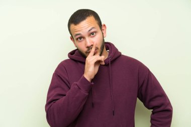 Yeşil duvar üzerinde sweatshirt ile Kolombiyalı adam sessizlik jest yapıyor
