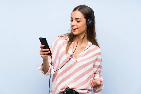 Mujer Joven Escuchando Música Con Móvil Sobre Una Pared Azul —  Fotos de Stock