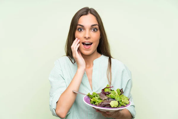 Young woman with salad over isolated green wall with surprise and shocked facial expression