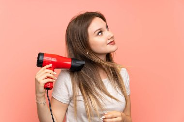 Saç kurutma makinesi ile pembe arka plan üzerinde Genç kız