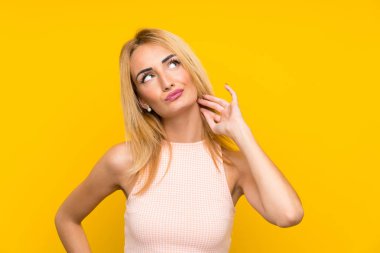 Genç Sarışın kadın üzerinde izole sarı duvar düşünme bir fikir