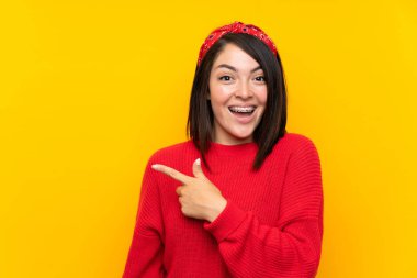 Yan parmak işaret sarı duvar üzerinde kırmızı kazak ile genç Meksikalı kadın