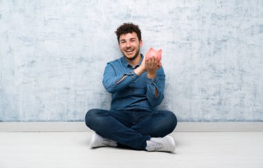 Yerde oturan genç adam elinde büyük bir kumbarayla