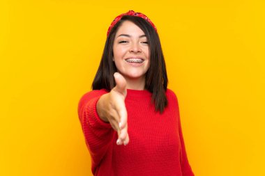 İyi bir anlaşma dan sonra sarı duvar el sıkışma üzerinde kırmızı kazak ile genç Meksikalı kadın