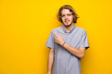 Bir ürün sunmak için yan işaret izole sarı arka plan üzerinde sarışın adam