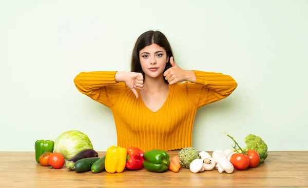 Teenager girl with many vegetables making good-bad sign. Undecided between yes or not