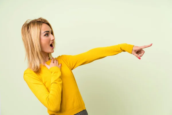 孤立した緑色の背景の上に若いブロンドの女性は 側面に指を指さす — ストック写真