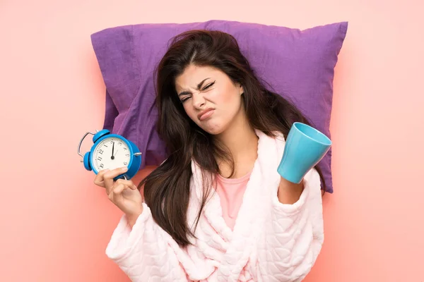 青少年女孩在睡衣在粉红色的后沟和强调持有老式时钟和拿着一杯咖啡 — 图库照片