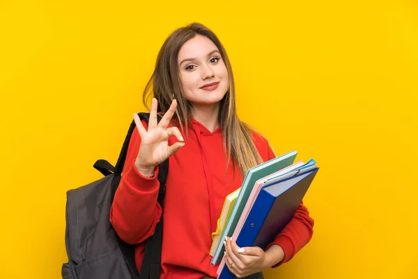 指でOkサインを示す黄色の背景の上にティーンエイジャーの学生の女の子 — ストック写真