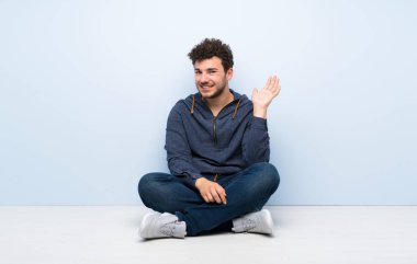 Mutlu ifade ile el ile selamlayan katta oturan genç adam