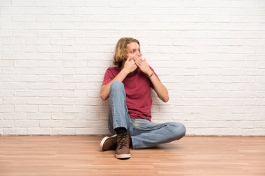 Sarışın adam yerde oturan ağız kapsayan ve yan bakıyor