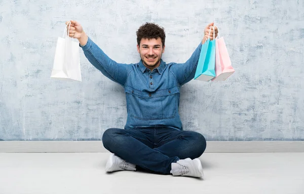 Yerde Oturan Genç Adam Elinde Bir Sürü Alışveriş Çantasıyla — Stok fotoğraf