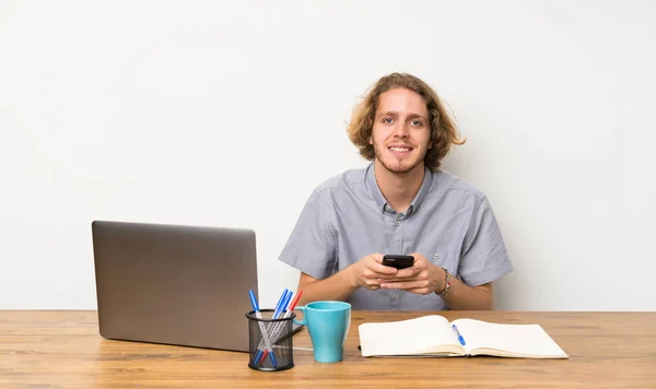 Blonde man with a laptop sending a message with the mobile