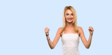 Genç sarışın kadın izole mavi arka plan üzerinde kazanan pozisyonda bir zafer kutluyor