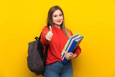 Genç öğrenci kız üzerinde sarı arka plan veren bir thumbs yukarı jest