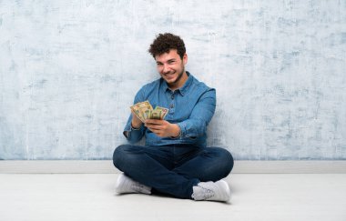 Yerde oturan ve çok para alan genç adam.
