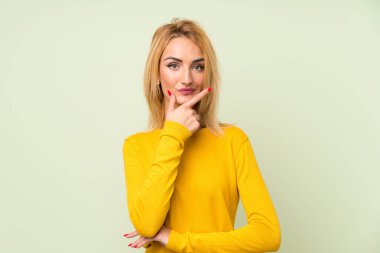 İzole yeşil arka plan üzerinde genç sarışın kadın bir fikir düşünme