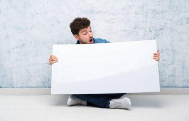 Genç adam bir kavram eklemek için boş bir beyaz pankart tutarak katta oturan