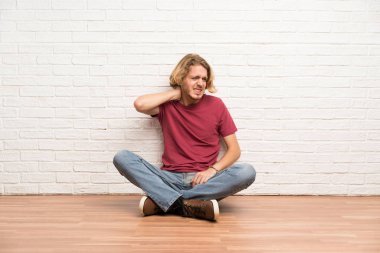 Sarışın adam boyun ağrısı ile yerde oturuyor