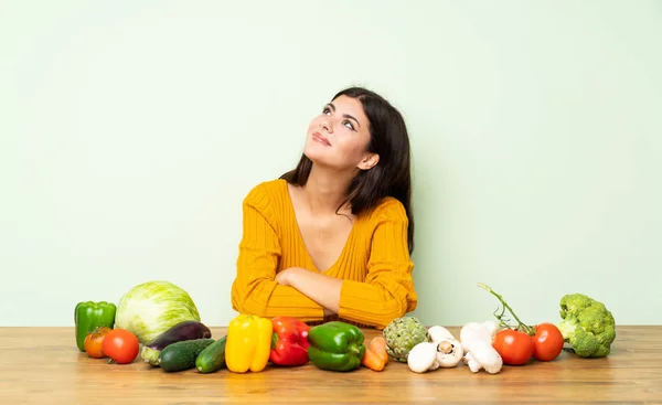 Teenager girl with many vegetables looking up while smiling