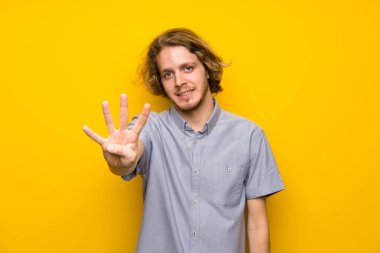 İzole sarı arka plan üzerinde sarışın adam mutlu ve parmak ile dört sayma