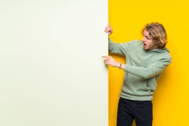 Büyük bir boş plasard tutan sarışın adam tarafına parmak işaret