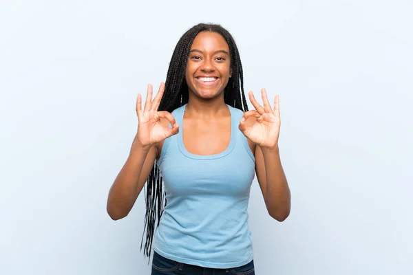 非裔美国少女与长辫子的头发在孤立的蓝色背景显示一个确定的标志与手指 — 图库照片