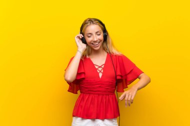 Izole sarı arka plan üzerinde Sarışın genç kadın kulaklık ile müzik dinlerken