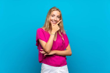 Izole mavi arka plan üzerinde Sarışın genç kadın gülümseyerek
