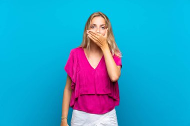 Elleriyle ağız kapsayan izole mavi arka plan üzerinde Sarışın genç kadın