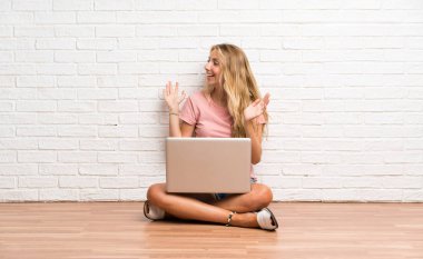 Sürpriz yüz ifadesi ile katta bir dizüstü bilgisayar ile genç sarışın öğrenci kız