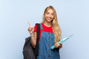 Izole mavi duvar üzerinde genç sarışın öğrenci kadın yan parmak işaret