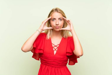 Izole yeşil arka plan üzerinde Sarışın genç kadın mutsuz ve bir şey ile sinirli. Negatif yüz ifadesi